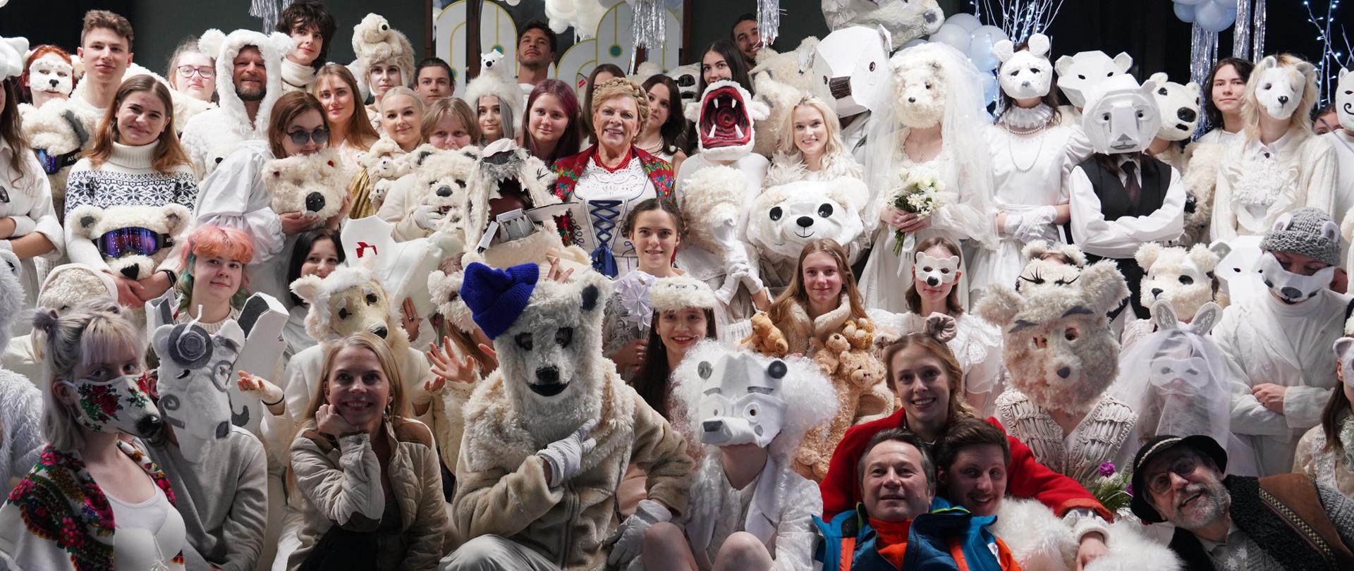 Na zdjęciu widzimy jedno z ujęć, kadr z filmu pt. "Poskromienie Złośnicy 2" w reżyserii Filipa Zylbera. Na zdjęciu uczniowie PLSP im. A. Kenara w Zakopanem wraz z aktorami biorącymi udział w filmie: Magdaleną Lamparską, Mikołajem Roznerskim, Agatą Turkot, Piotrem Nerlewskim, Tomaszem Saprykiem, Piotrem Cyrwusem, Elżbietą Trzaskoś, Janem Kardasińskim, Martinem Budnym i Patricią Kazadi. Fot.: Maria Majerczyk. Uczniowie i aktorzy, wszyscy przebrani są za białe misie, biorą udział w balu białego misia. Fotografia została wykonana w sali Teatru Witkacego w Zakopanem.