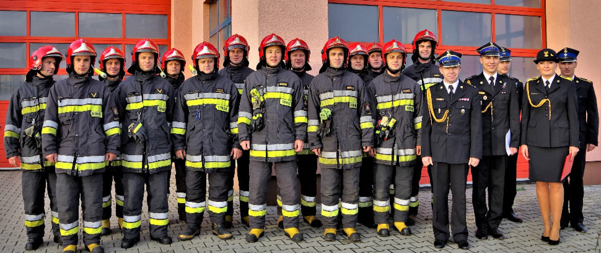 grupa strażaków w umundurowaniu na tle czerwonych bram garażowych