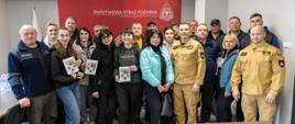 Ósma wizyta studyjna ukraińskich strażaków ochotników, samorządowców i pracowników gmin odpowiedzialnych za obronę cywilną. Przyjechali do Polski szkolić się – poznać funkcjonowanie struktur Ochotniczej i Państwowej Straży Pożarnej w Polsce - aby na ich wzór zapoczątkować i rozszerzać ochotnicze pożarnictwo na swoim terenie. Wspólne zdjęcie. W tle banner Państwowej Straży Pożarnej koloru czerwonego z białym napisem i logiem Państwowej Straży Pożarnej. Widoczne również Flagi Rzeczypospolitej Polskiej.