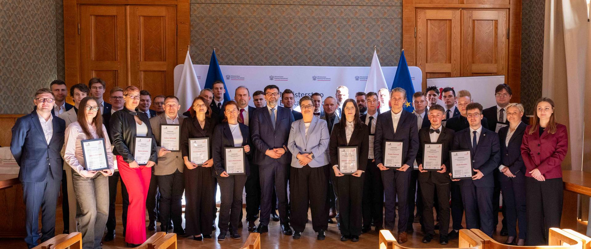 Na zdjęciu kadra, która została powołana przez wiceminister na WorldSkills 2026. Wszyscy wraz Sekretarz Stanu Katarzyną Lubnauer stoją na tle ścianki Ministerstwa Edukacji Narodowej. 