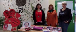 Za stołem z materiałami edukacyjnymi stoją trzy kobiety, z boku wystawa z serc z napisem „Nie daj szansy AIDS”.