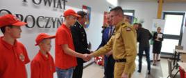 Zastępca KG PSP podaje rękę w geście gratulacji chłopcu – członkowi MDP, obok którego stoi dwóch chłopców, w tle inni uczestnicy. 