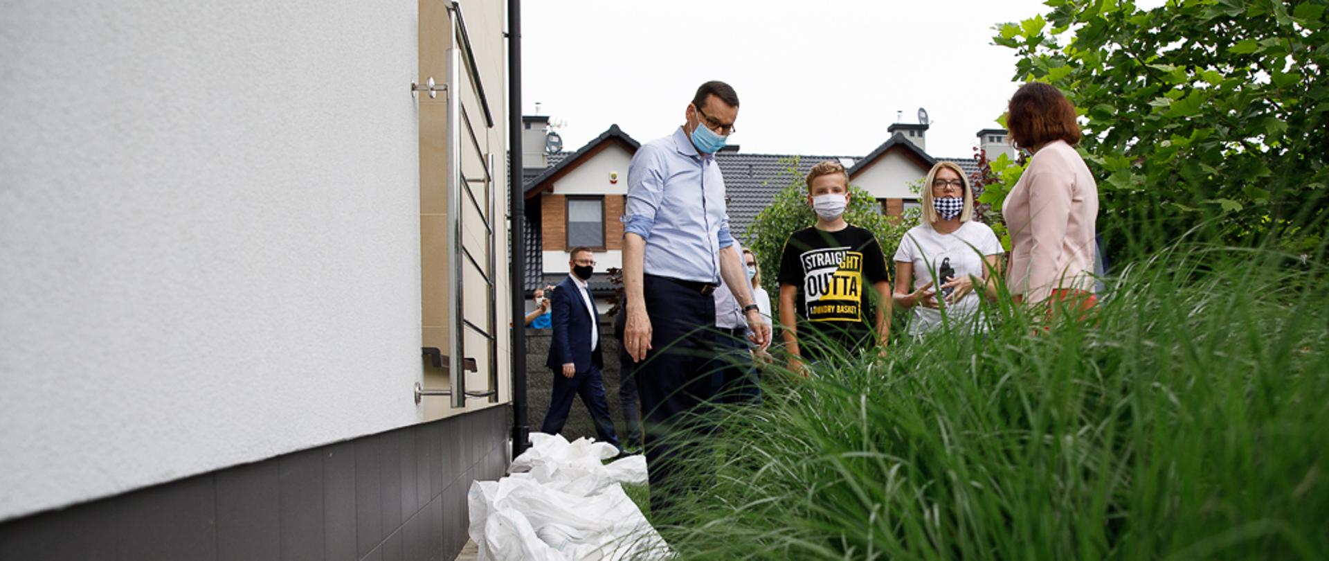 Premier Mateusz Morawiecki patrzy na zabezpieczenie domu workami z piaskiem.