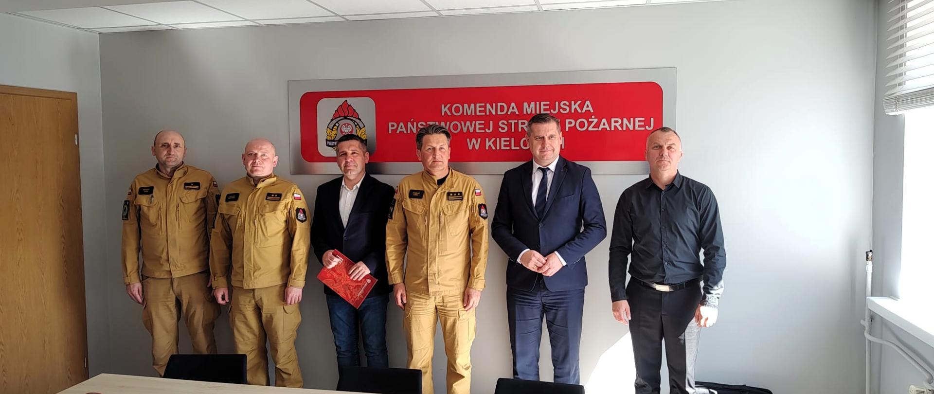 Fotografia przedstawia funkcjonariuszy Komendy Miejskiej PSP w Kielcach, burmistrza Chmielnika i druhów OSP Śladków Mały ustawionych do pamiątkowego zdjęcia podczas przekazania samochodu kwatermistrzowskiego.