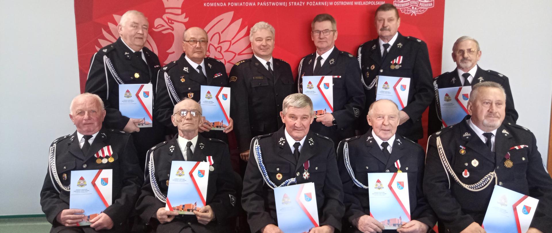 Druhowie ustawieni w dwóch rzędach z teczkami w rękach, wśród nich Komendant Powiatowy PSP.