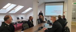 Druhowie OSP w mundurach wyjściowych w trakcie prezentacji założeń ustawy o OSP na sali konferencyjnej.