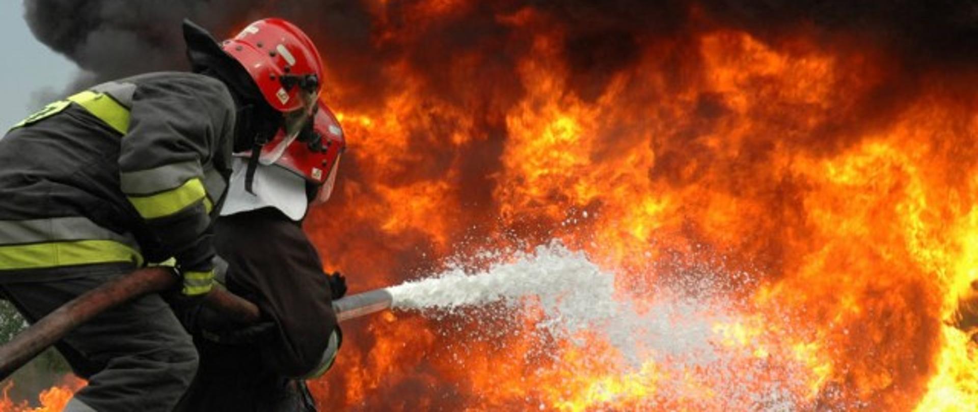 Dwóch strażaków podaje prąd gaśniczy piany ciężkiej na pożar