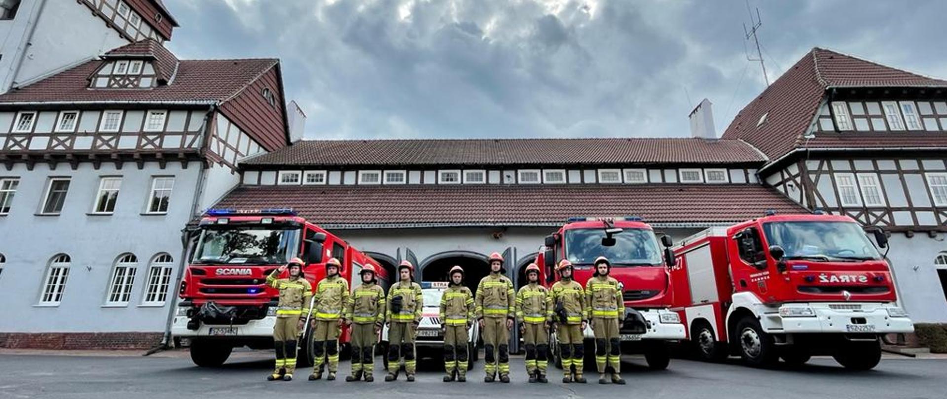 Strażacy stoją przed pojazdami pożarniczymi i przed Komendą Miejską Państwowej Straży Pożarnej w Zabrzu.