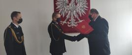 Zdjęcie przedstawia zastępcę pomorskiego komendanta wojewódzkiego PSP wręczającego decyzję o przejściu na emeryturę.