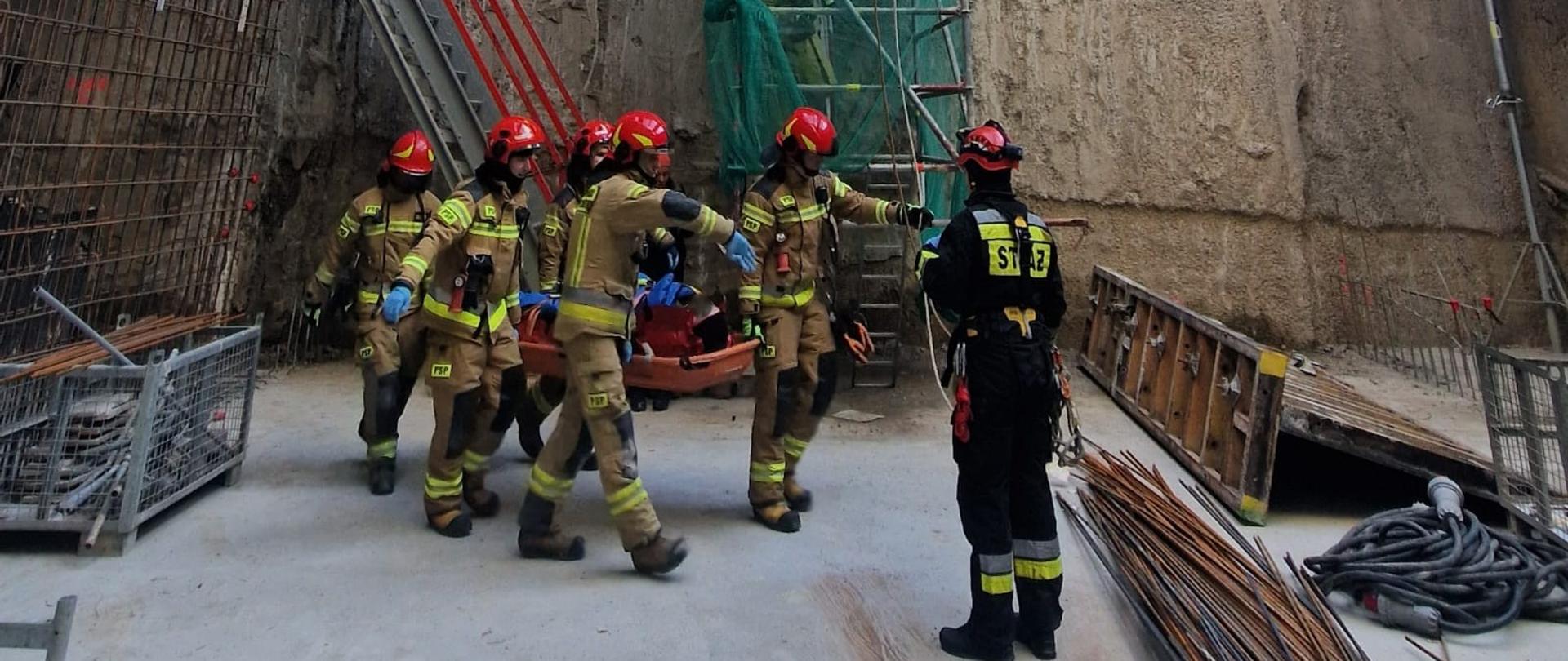 Na zdjęciu widać moment przenoszenia noszy z poszkodowanym przez strażaków zabezpieczających przebieg ewakuacji.
