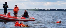 Zdjęcie przedstawia strażaków podczas ćwiczeń na zbiorniku Jeziorsko, w wodzie znajdują się 3 osoby. Strażacy wyciągają jedną osobę poszkodowaną przy pomocy linki z węgorzem ratowniczym. 
