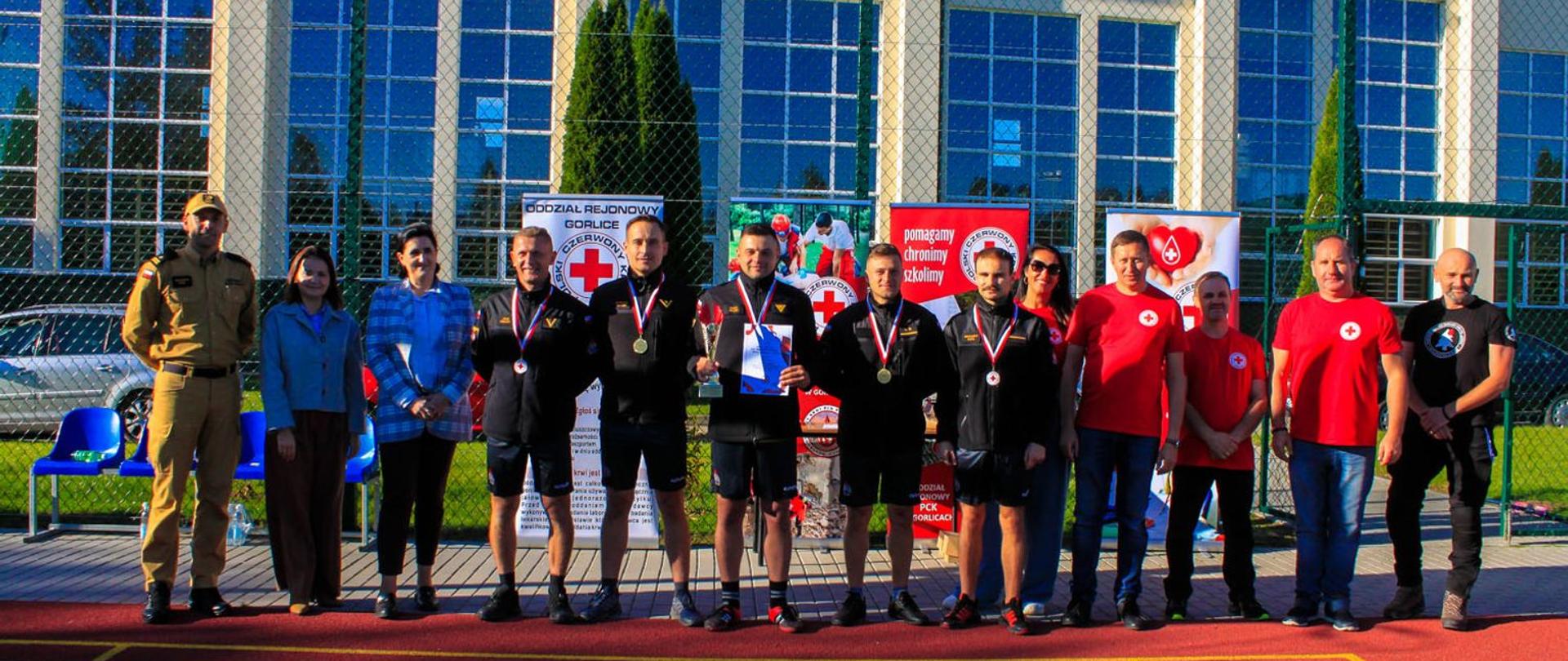 Na zdjęciu widoczni strażacy z Klubu Honorowych Dawców Krwi Polskiego Czerwonego Krzyża przy KP PSP w Gorlicach zwycięzcy XXXIII Spartakiady HDK PCK w Brunarach wraz zaproszonymi gośćmi i zarządem Oddziału Rejonowego Polskiego Czerwonego Krzyża w Gorlicach. W tle rollupy promujące ruch Polskiego Czerwonego Krzyża i budynek szkoły.
