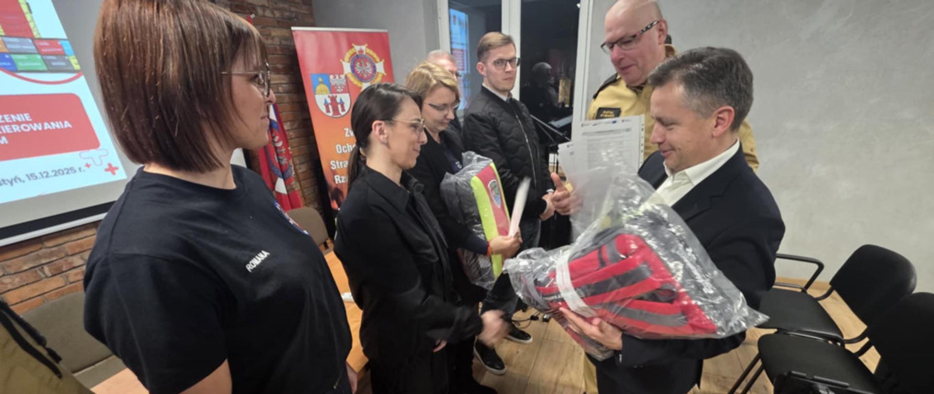 Starosta i komendant wręczają plecaki ratownicze.