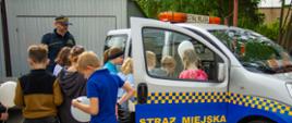 Grupa dzieci ogląda z bliska samochód Straży Miejskiej podczas dnia otwartego