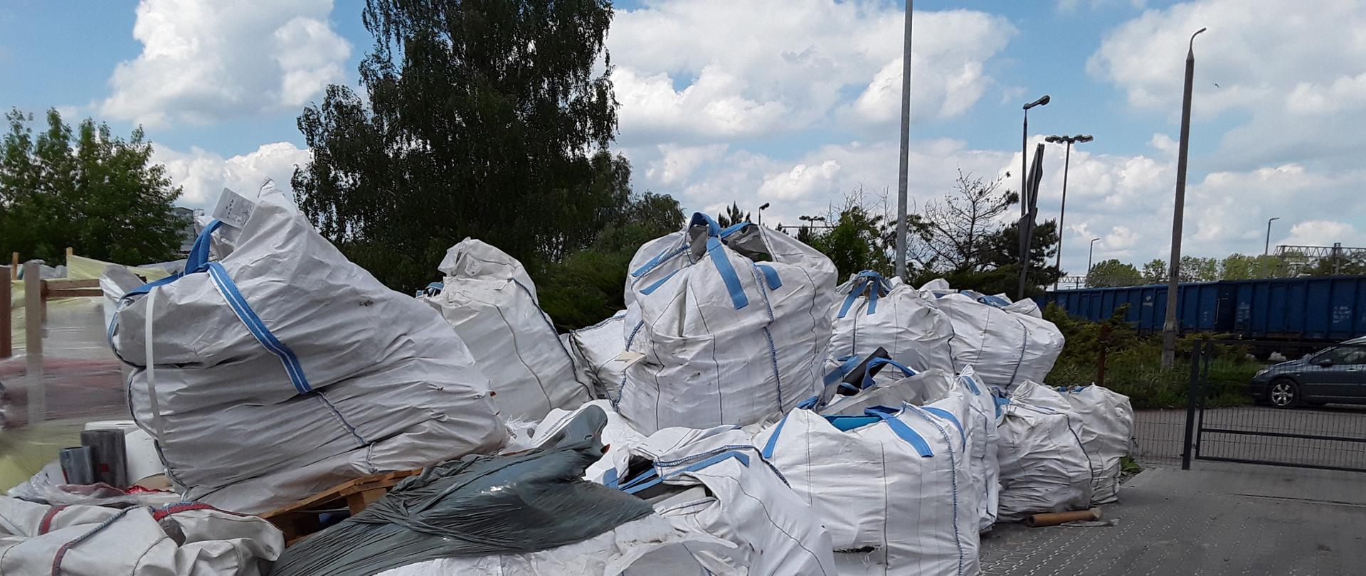Plac pokryty kostką brukową, na nim na paletach ustawione są worki typu big-bag wypełnione odpadami wysłanymi z Niemiec