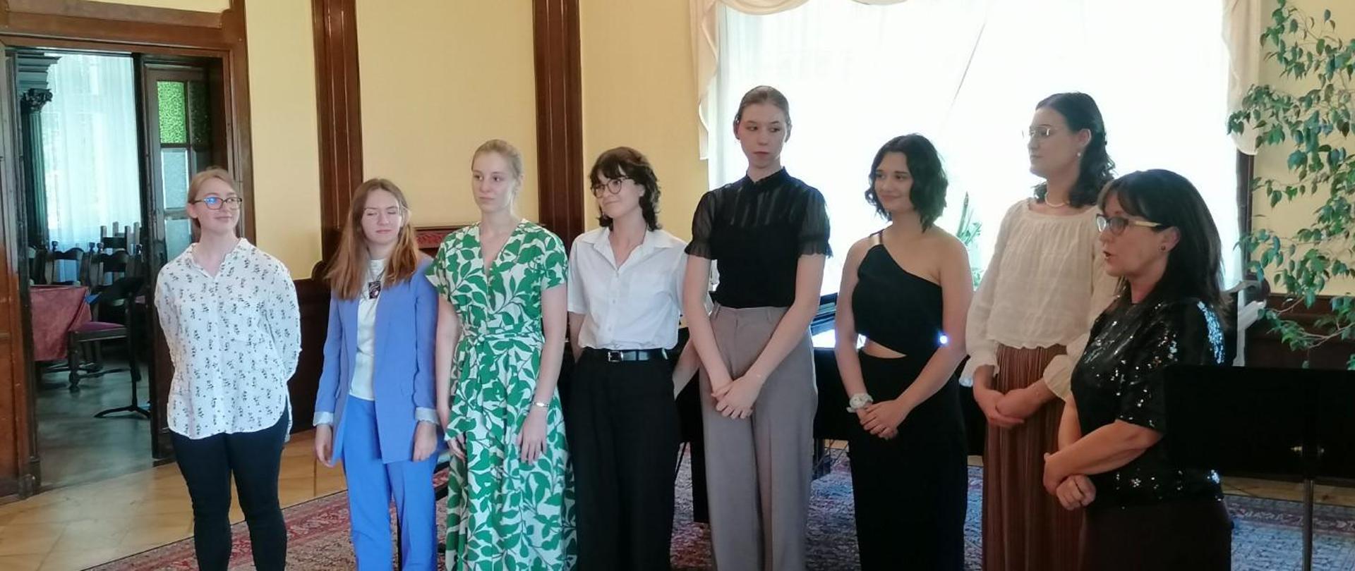 Zdjęcie kolorowe - grupa osób stojących na scenie w strojach galowych. 