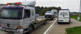 Zatrzymana do kontroli srebrna ciężarówka z przyczepą na której stoi samochód. Obok radiowóz ITD.