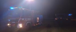 Zdjęcie w porze nocnej. Oświetlenie sztuczne. Widać teren działań ratowniczo-gaśniczych oraz pojazd ratowniczo-gaśniczy.