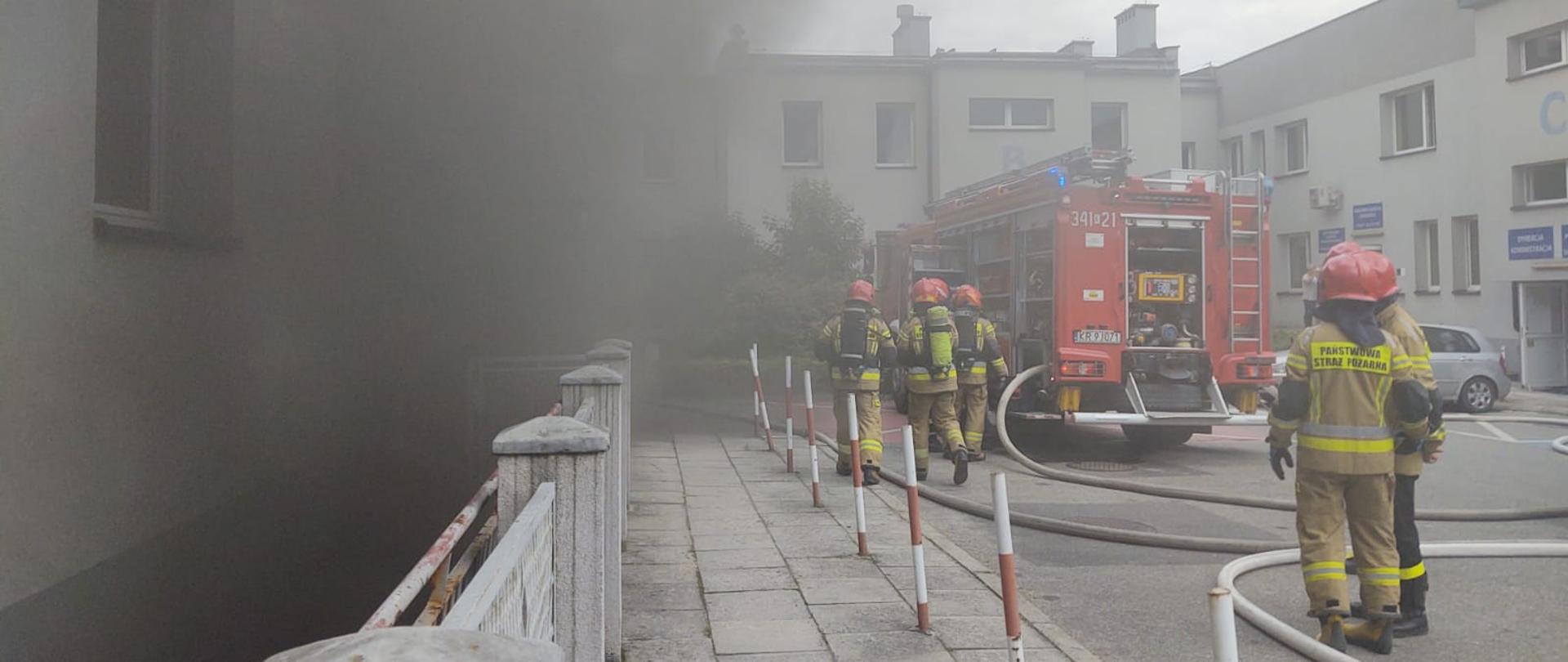 Dym wydobywający się z przychodni oraz strażacy i samochody pożarnicze w dzianiach. 