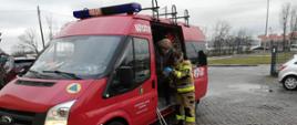 Zdjęcie przedstawia wóz strażacki który przewozi osobę starszą