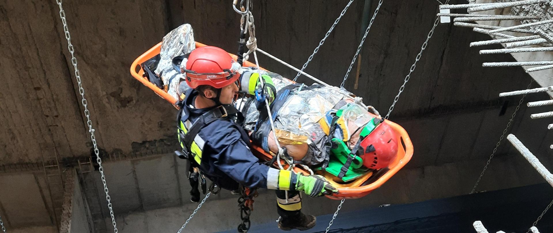 Strażak wiszący na linie wraz z noszami podczas ewakuacji poszkodowanego z tunelu