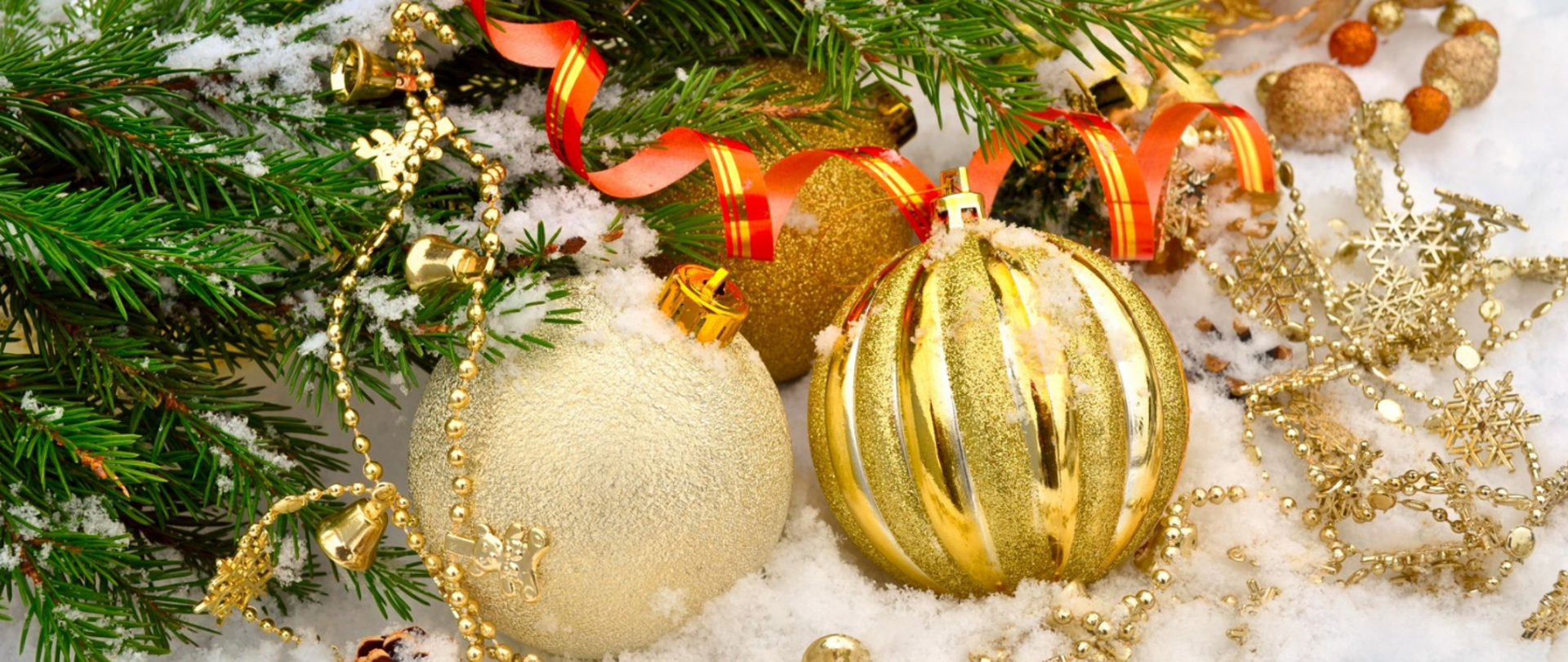 Na śniegu, na pierwszym planie trzy złote bombki, złoty łańcuch z dzwoneczkami i złotymi śnieżynkami, z lewej strony gałązka świerku, czerwono-złota wstążka. Z prawej strony kilka małych bombek. 