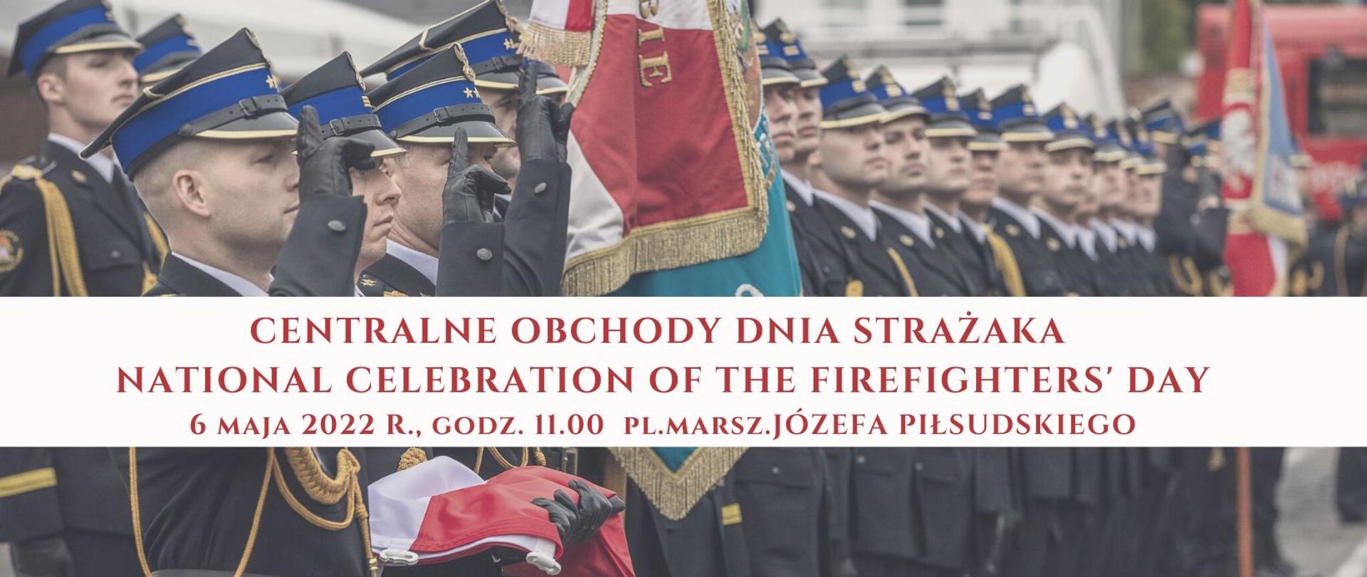 Na zdjęciu widać strażaków PSP w mundurach galowych, na pierwszym planie poczet sztandarowy. Napis na zdjęciu: Centralne Obchody Dnia Strażaka. National celebration of the firefighters' day. 6 maja 2022 roku godz. 11.00 plac Marszałka Józefa Piłsudskiego 