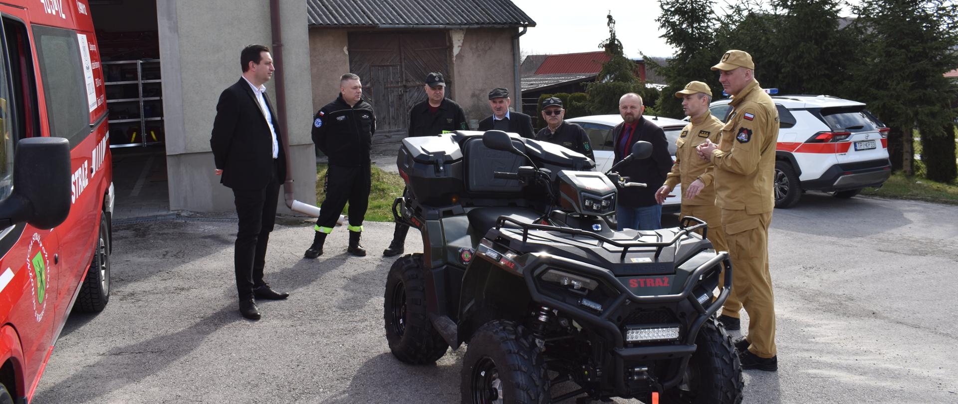 Komendanci PSP i strażacy OSP stojący obok pojazdu quad z jednostki OSP Kije. 