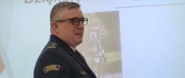 Zastępca Komendanta Wojewódzkiego st. bryg. Rafał Świerczek przemawia do uczestników narady. W tle prezentacja multimedialna.