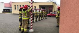 Strażacy Państwowej Straży Pożarnej podpinają flagę, aby uroczyście podnieść ją na maszt.