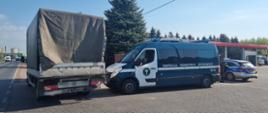 Od lewej: zaparkowany na poboczu drogi samochód dostawczy. Obok zatrzymanego do kontroli pojazdu stoi oznakowany furgon mazowieckiej Inspekcji Transportu Drogowego i oznakowany radiowóz Policji. Policjanci ruchu drogowego prowadzą czynności z ujętym kierowcom busa w stanie wskazującym na spożycie alkoholu.