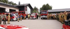 Zdjęcie przedstawia strażaków ustawionych na zbiórce, widać również ustawione wozy strażackie. W tle remiza OSP Gołubie