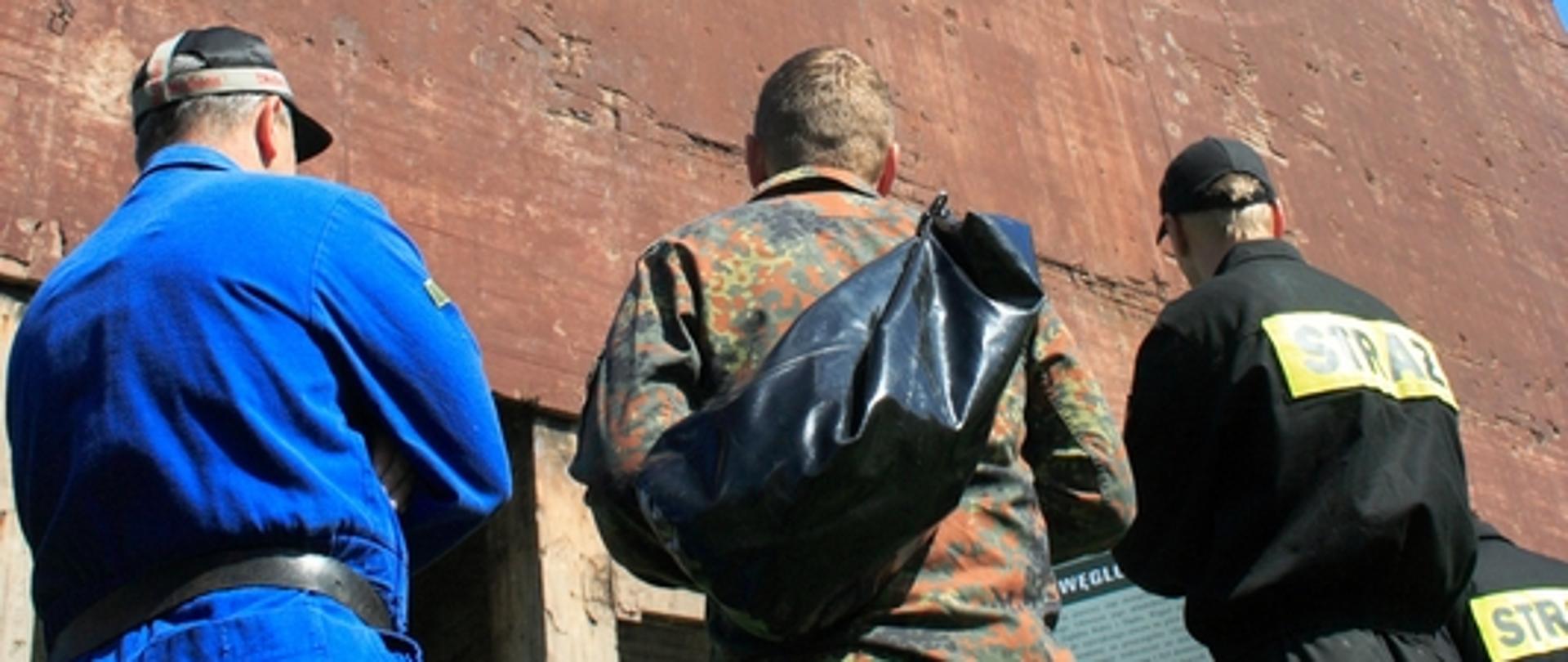 Zdjęcie przedstawia strażaków przed zniszczonym budynkiem