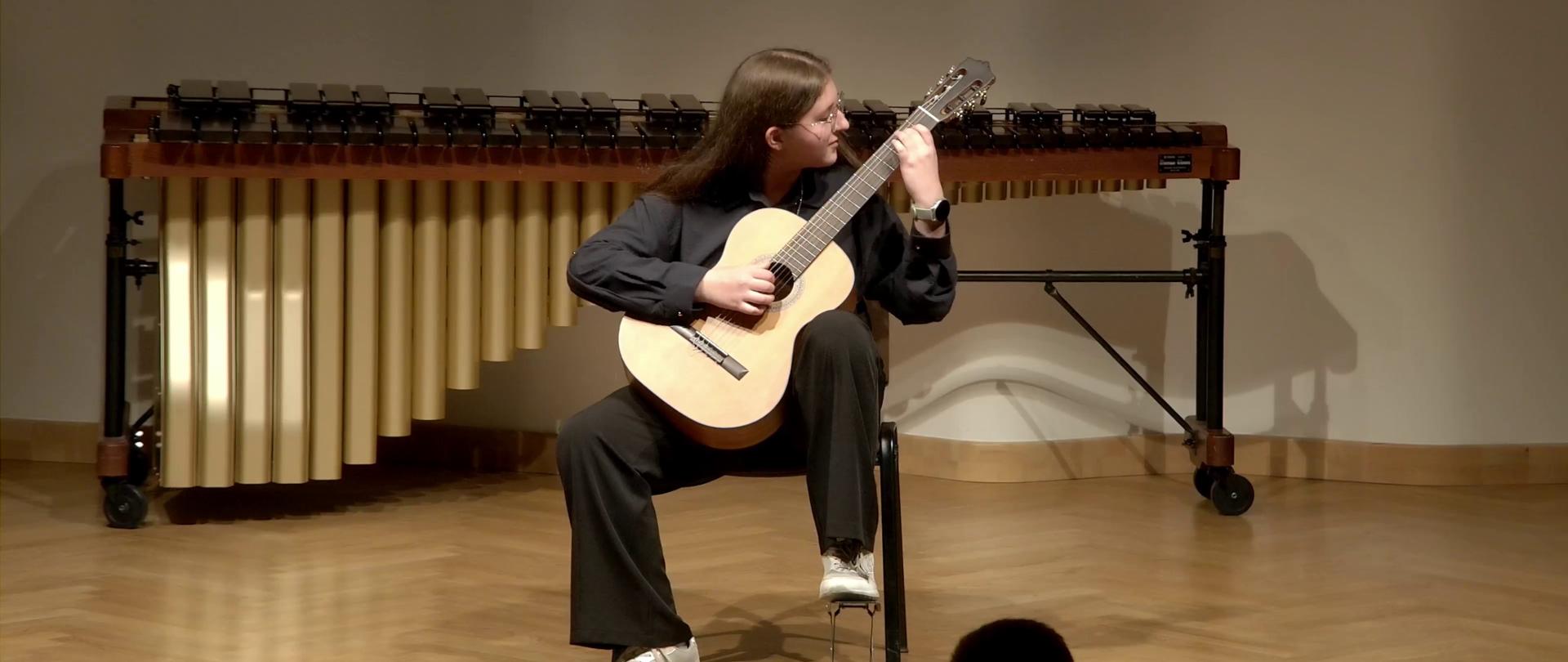 Zdjęcie. na estradzie Sali Koncertowej występuje gitarzystka. Za nią widać instrument perkusyjny - marimbę.