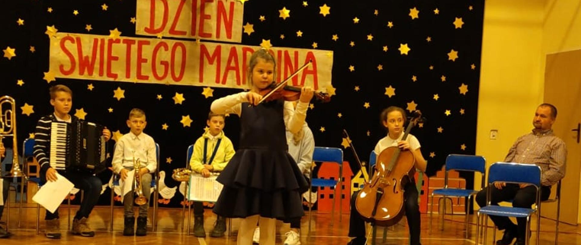 Zdjęcie przedstawia występ uczennicy grającej na skrzypcach oraz słuchających jej innych osób