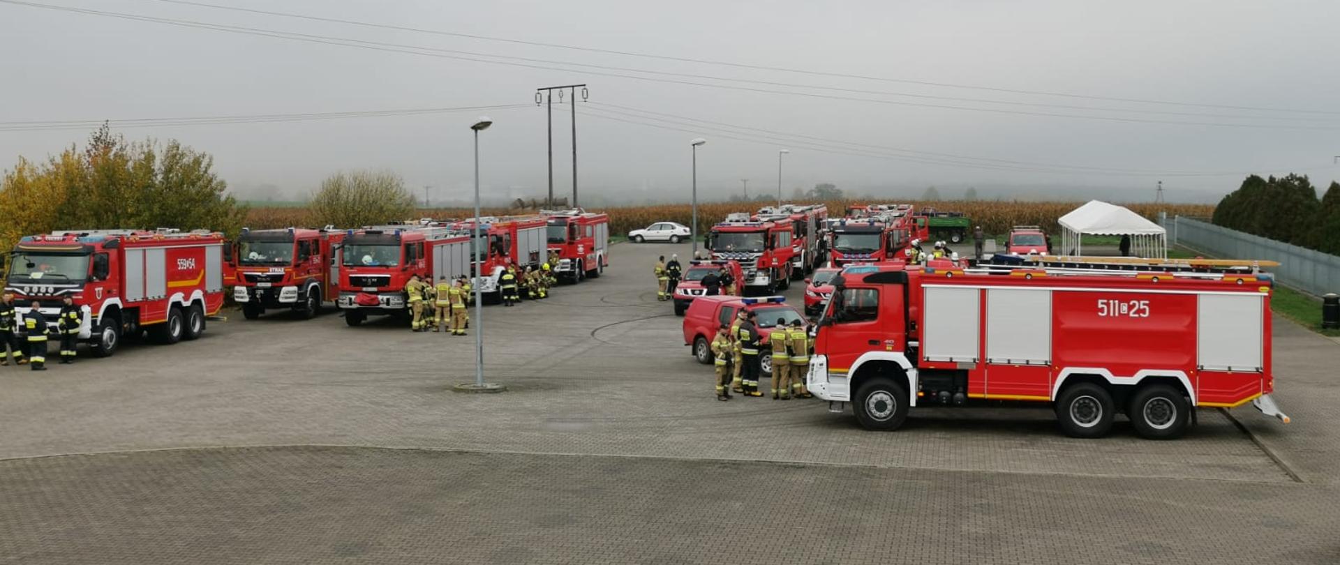 Samochody pożarnicze ciężarowe stoją na placu w punkcie przyjęcia sił i środków.