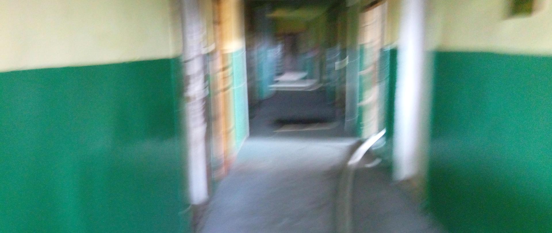 Zdjęcie przedstawia korytarz wewnętrzny bloku socjalnego przy ulicy Młodej w Kielcach i wąż gaśniczy leżący na podłodze. Wzdłuż korytarza widać drzwi do mieszkań. 