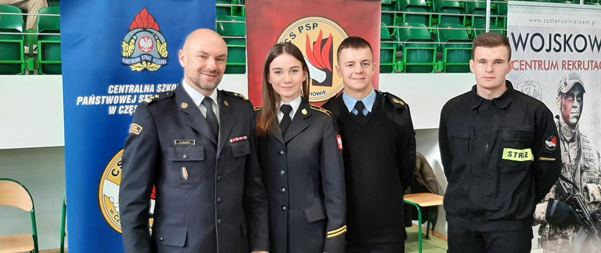 Czterech funkcjonariuszy w rzędzie. Od lewej: oficer CS PSP, kadetka oraz dwóch kadetów na tle banerów