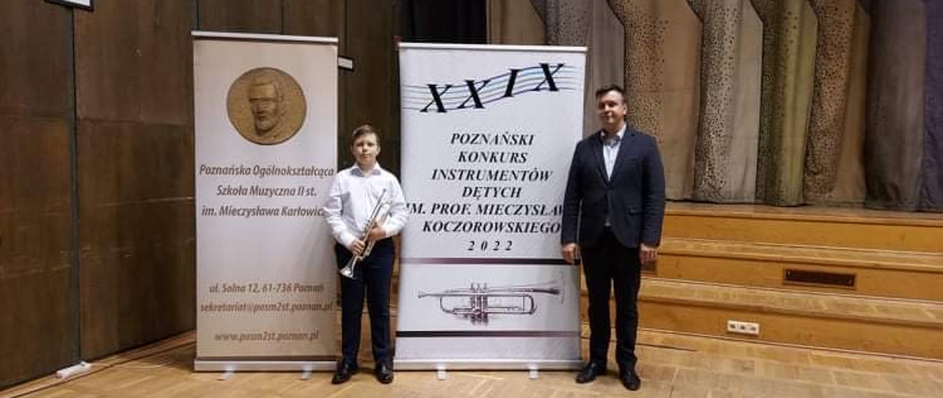 Laureat konkursu stoi z pedagogiem na tle baneru