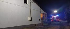 Zdjęcie w porze nocnej. Oświetlenie sztuczne. Widać teren działań ratowniczo-gaśniczych oraz pojazd ratowniczo-gaśniczy.