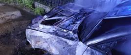 Zdjęcie przedstawia spalone auto. Auto koloru srebrnego. Auto ugaszone. Przód po pożarze w komorze silnika
