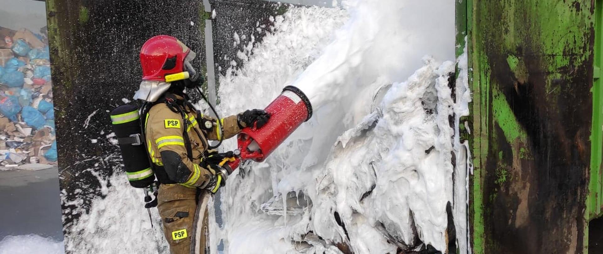zdjęcie przedstawia strażaka podającego pianę średnią na palące się materiały