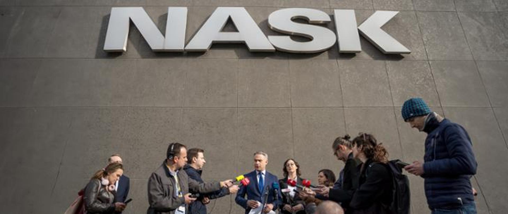 Zdjęcie uczestników konferencji prasowej - z premierem Gawkowskim. Nad dziennikarzami napis NASK