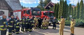 Zdjęci grupowe. Na pierwszym planie widać strażaków stojących w szeregu na tle samochodów pożarniczych. 