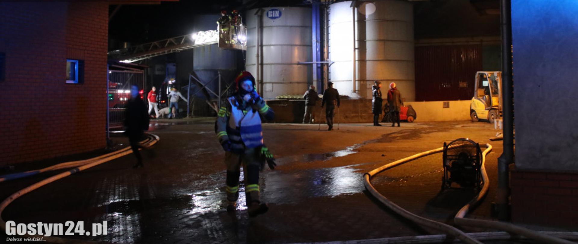 strażak idacy z radiostacją, w tle grupy ludzi i silosy