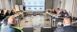 Międzynarodowe warsztaty Tachograph Fraud Masterclass w Belgii - widok ogólny na salę szkoleniową, w centrum wyświetlana na ekranie prezentacja i prowadzący wykład, a wkoło słuchający inspektorzy.