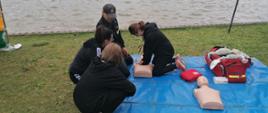 Na zdjęciu widać strażaka, oraz uczestników festyny podczas nauki pierwszej pomocy. W tle widać jezioro