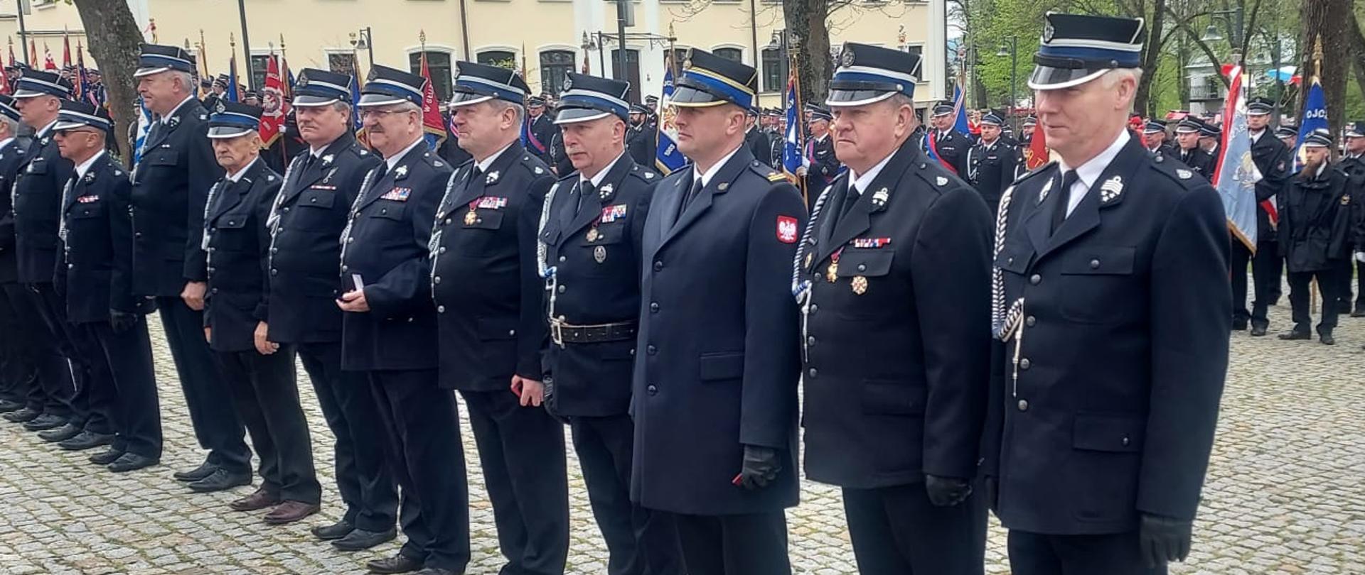 Na zdjęciu widać komendanta powiatowego PSP w Ustrzykach Dolnych oraz druhów OSP występujących w szyku w mundurach galowych. W tle widać poczty sztandarowe.