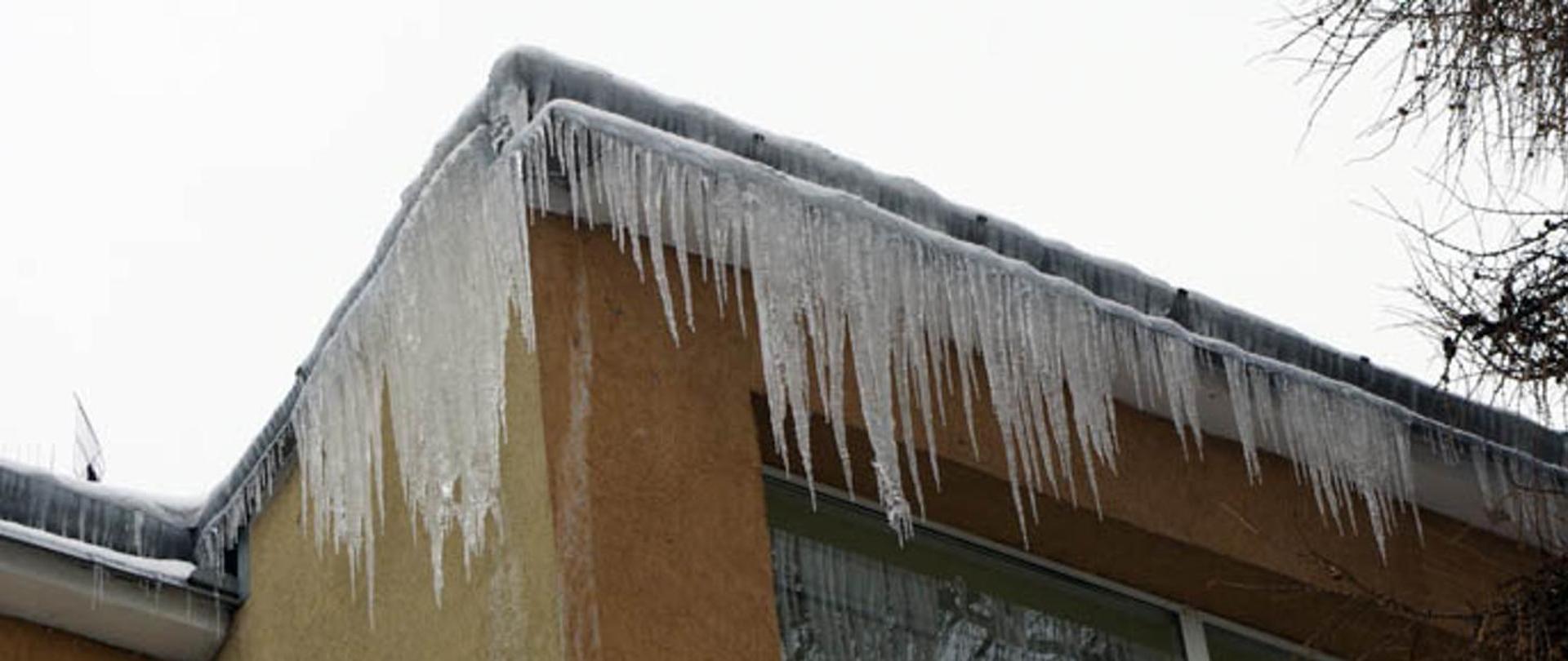zdjęcie przedstawia zwisające z dachu sople lodu 