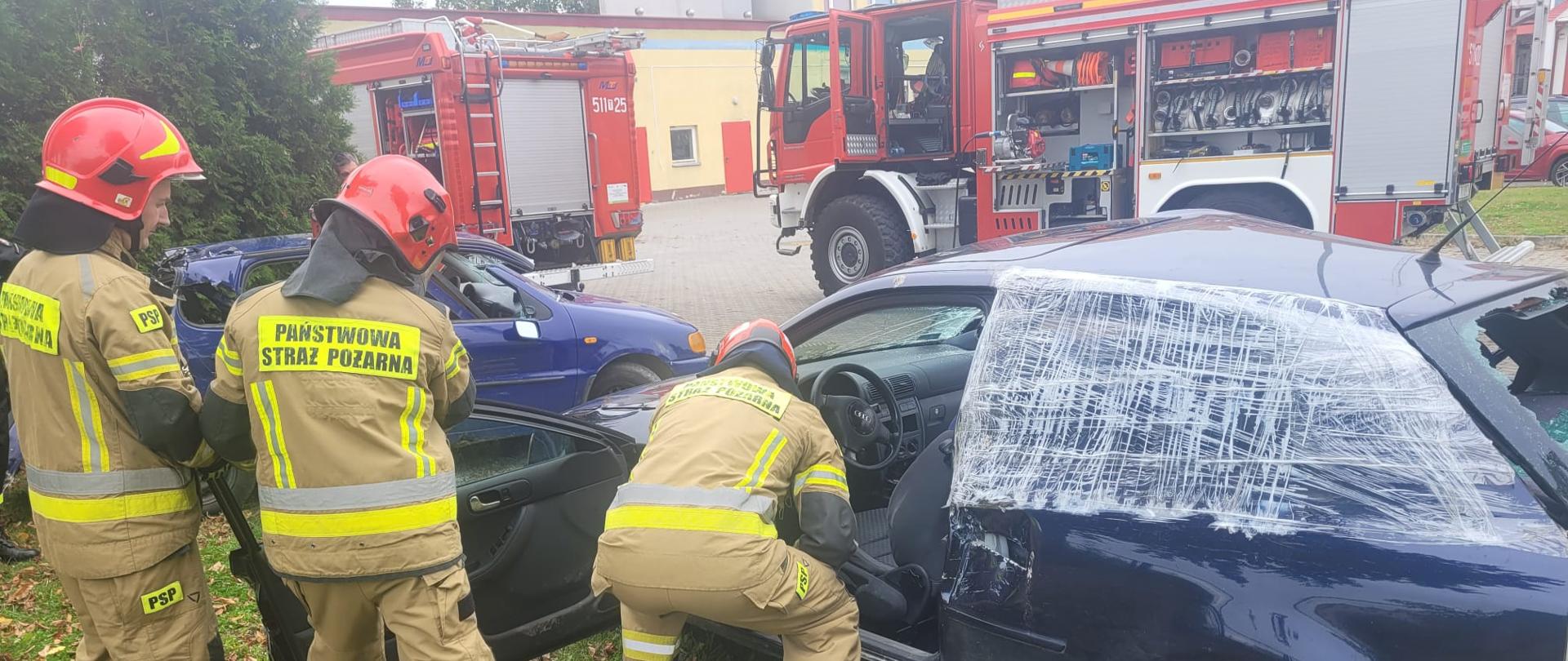 Plac wewnętrzny Komendy Powiatowej PSP we Włoszczowie. Strażacy dokonują oględzin uszkodzonego samochodu osobowego celem wybrania odpowiednich technik ratowniczych.